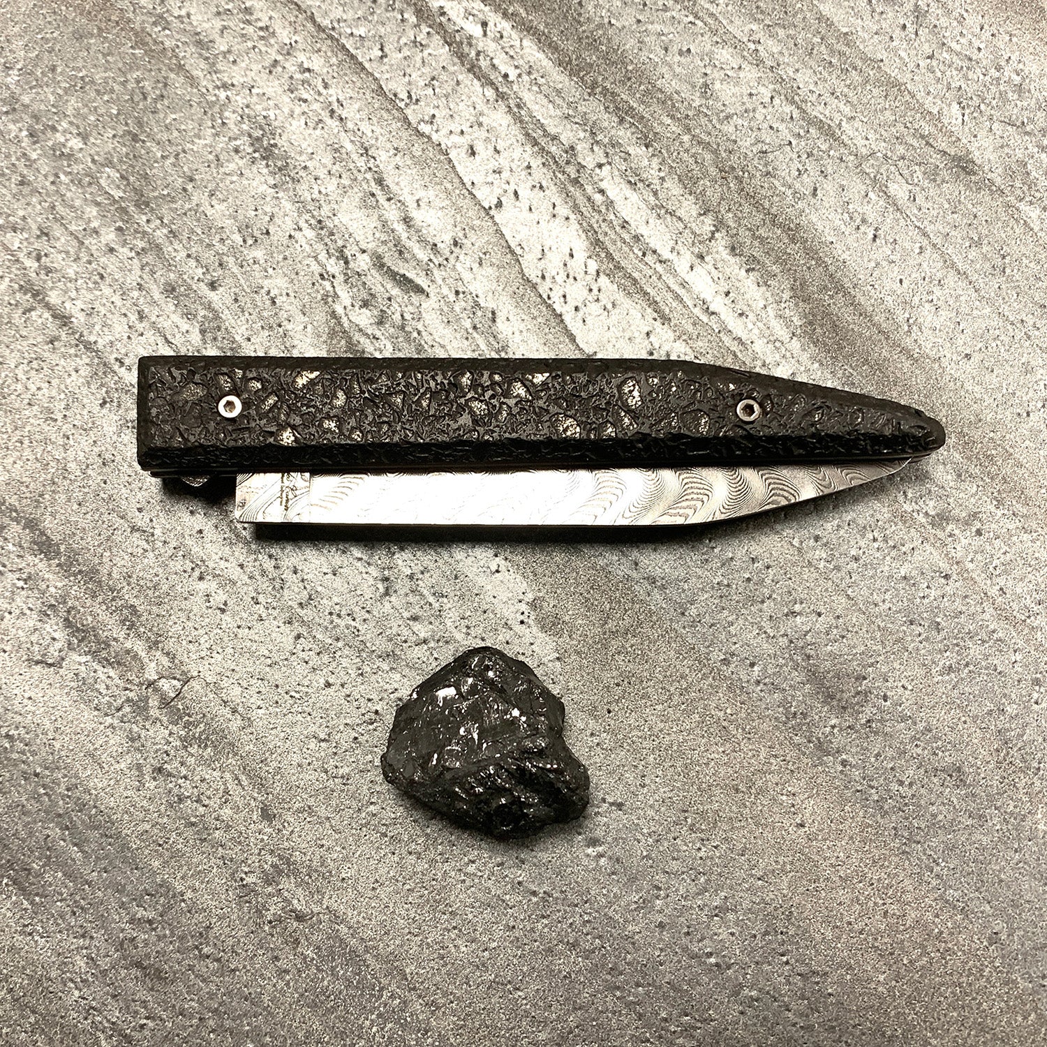 The slag heap: folding knife with raw charcoal handle and Damascus blade